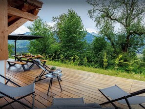 A wooden deck with a picnic table and lounge chairs, overlooking a forested area with mountains in the distance. - Chalet Lezopau - mountain break with spa and petanque - OVO Network (Samoëns)