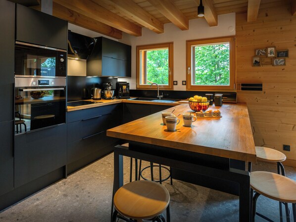 A modern kitchen with dark cabinetry, a wooden island, and a large window.