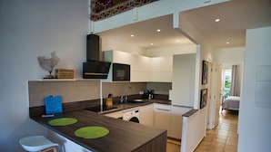 A modern kitchen with a central island, white bar stools, a microwave, and a washing machine. - Orient Parc - the best location (Saint martin)