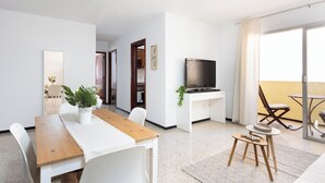 Een moderne woonkamer met een houten eettafel, witte stoelen, een televisie en een balkon met een stoel.