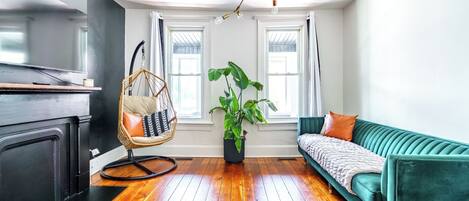 Una sala de estar moderna con un sofá verde, un sillón colgante, una planta en maceta y piso de madera.