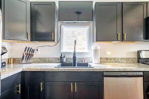 A kitchen with dark cabinets, a built-in dishwasher, and a window above the sink. - Jungle House Urban Lofts – Arena District & Short North (Columbus)