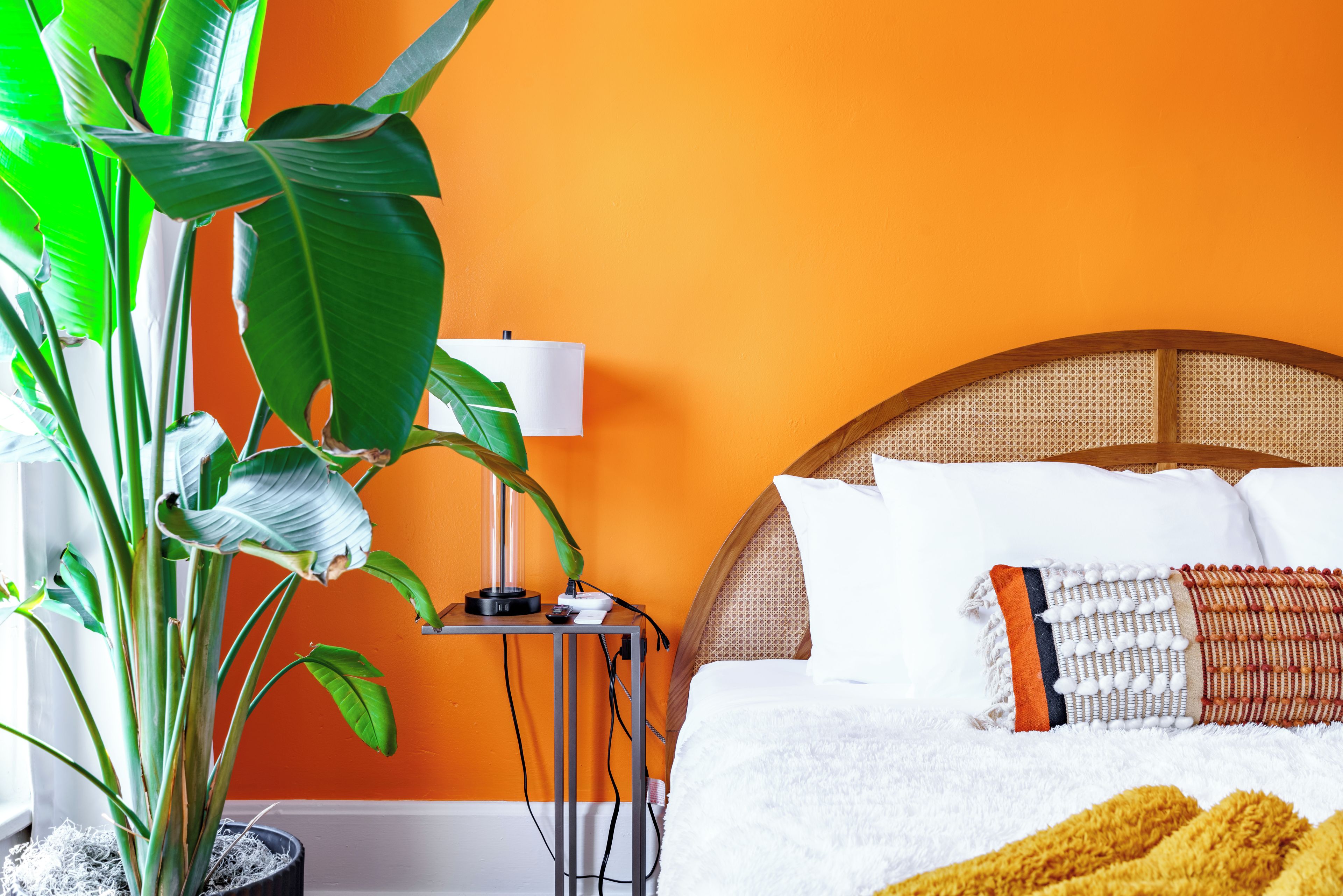A bed with white bedding, a yellow throw blanket, and a plant in a pot.