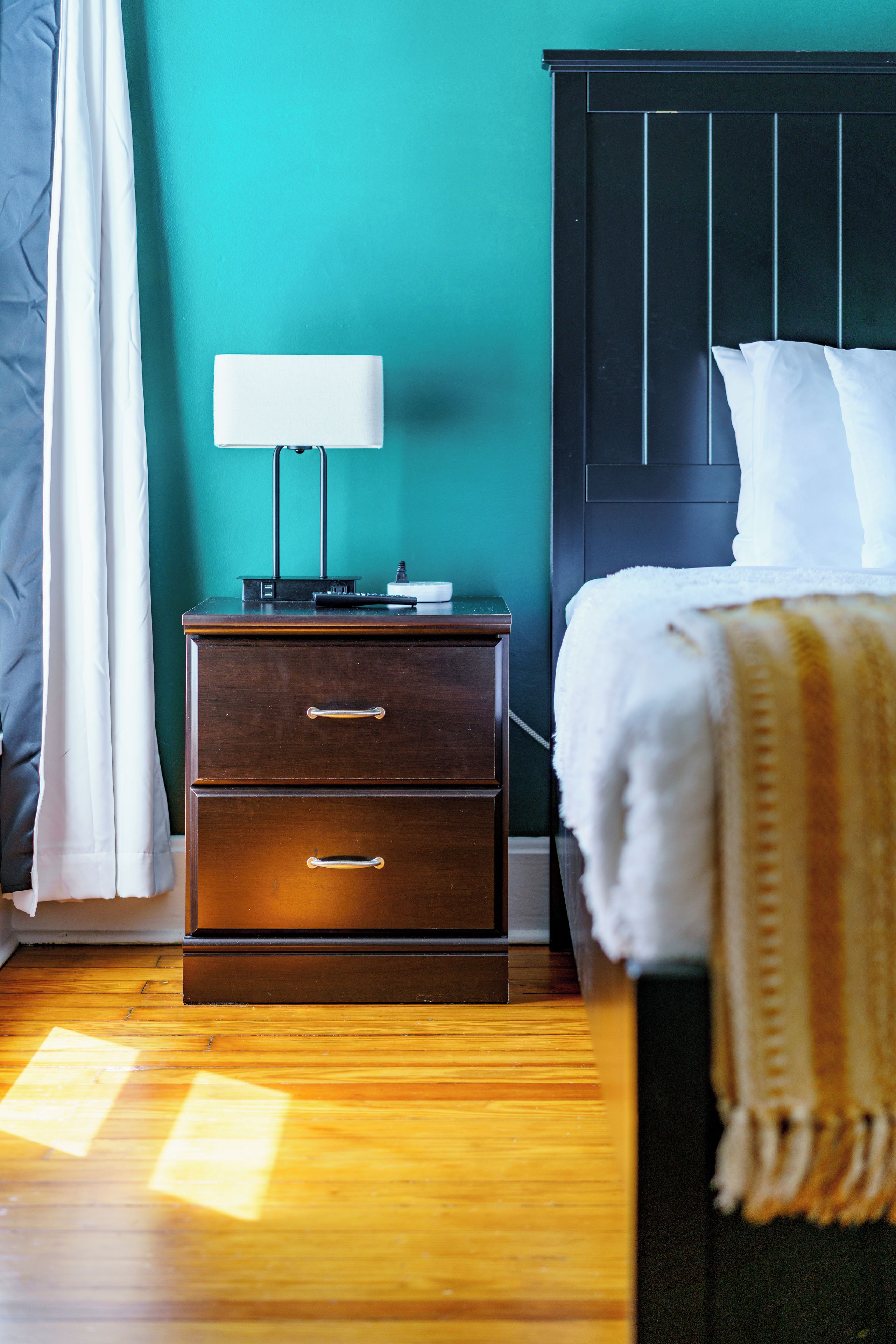 A bedroom with a bed, a nightstand with a lamp, and a wooden floor.