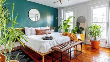 Een slaapkamer met een bed, een bankje, een spiegel en planten in potten.