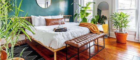 Une chambre à coucher avec un lit, un banc, un miroir et des plantes en pot.