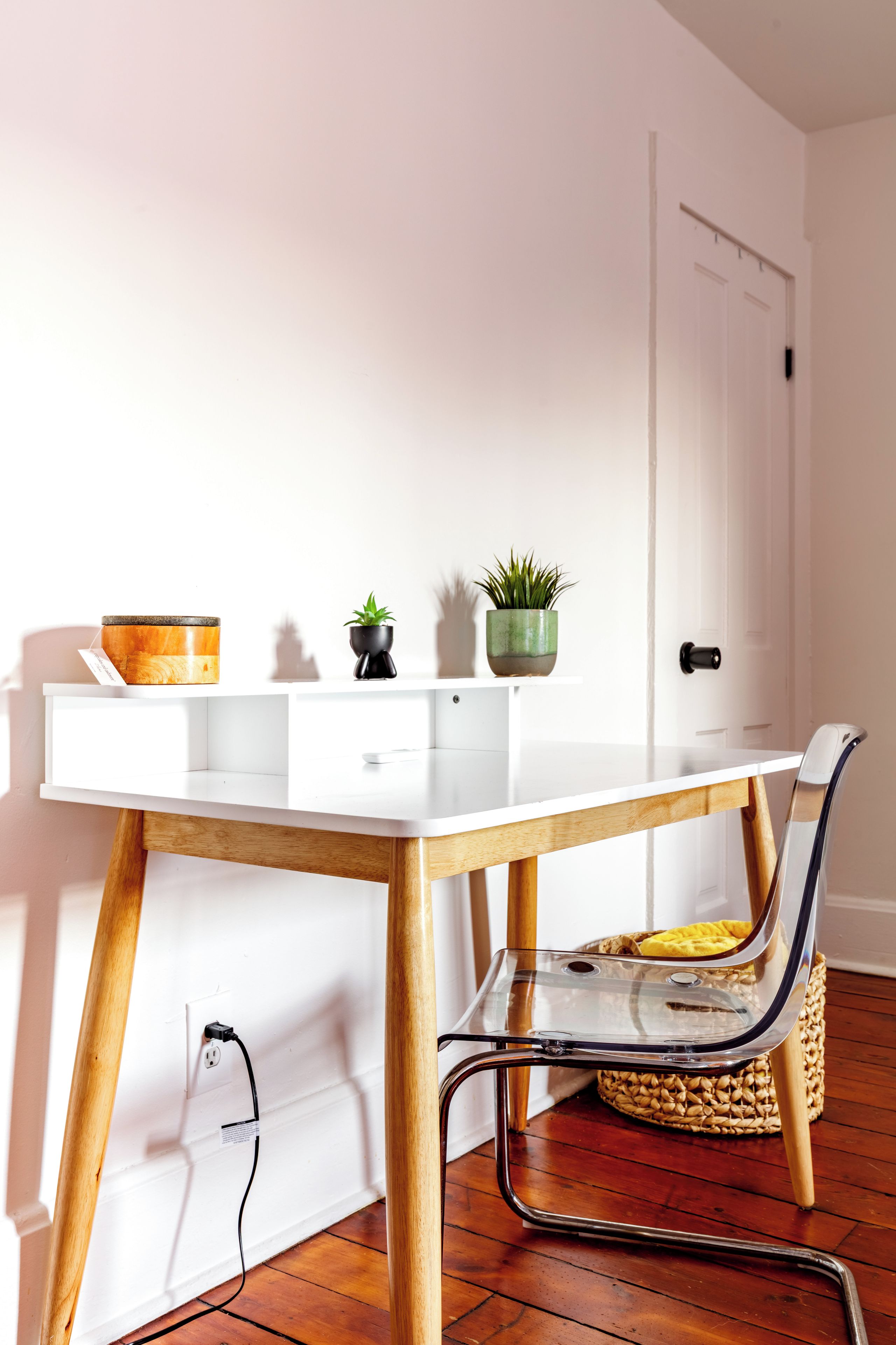 Un bureau blanc avec un plateau en verre, des pieds en bois et une chaise avec une structure en métal. Deux plantes en pot sont posées sur le bureau.