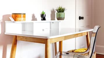 A white desk with a glass top, wooden legs, and a chair with a metal frame. There are two potted plants on the desk.