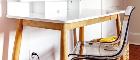 A white desk with a glass top, wooden legs, and a chair with a metal frame. There are two potted plants on the desk.