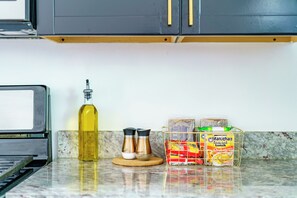 A kitchen counter with a bottle of oil, two salt and pepper shakers, and a lunchbox containing snacks.