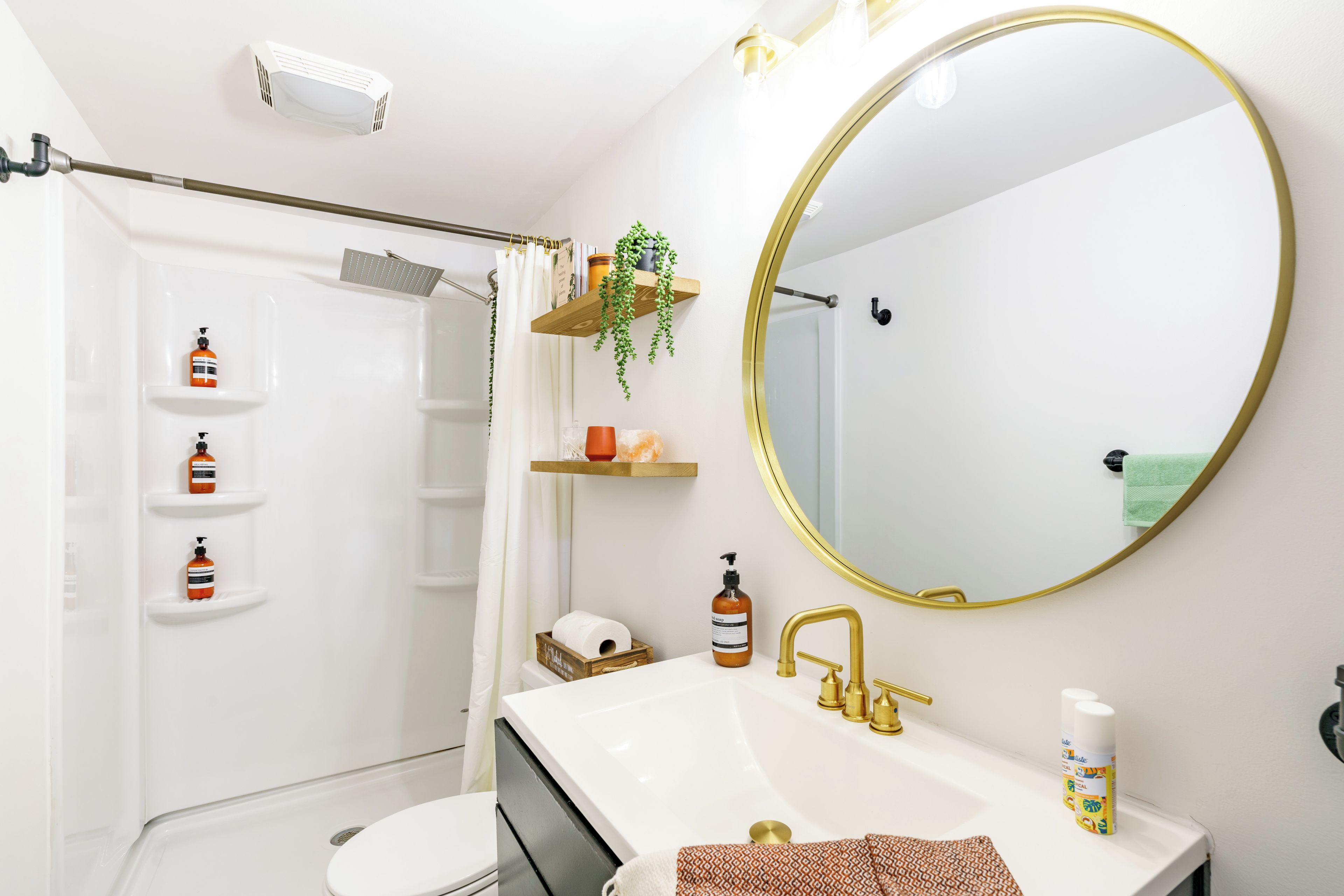 Een badkamer met een witte wastafel, gouden kraanwerk, een grote spiegel en planken met toiletartikelen.