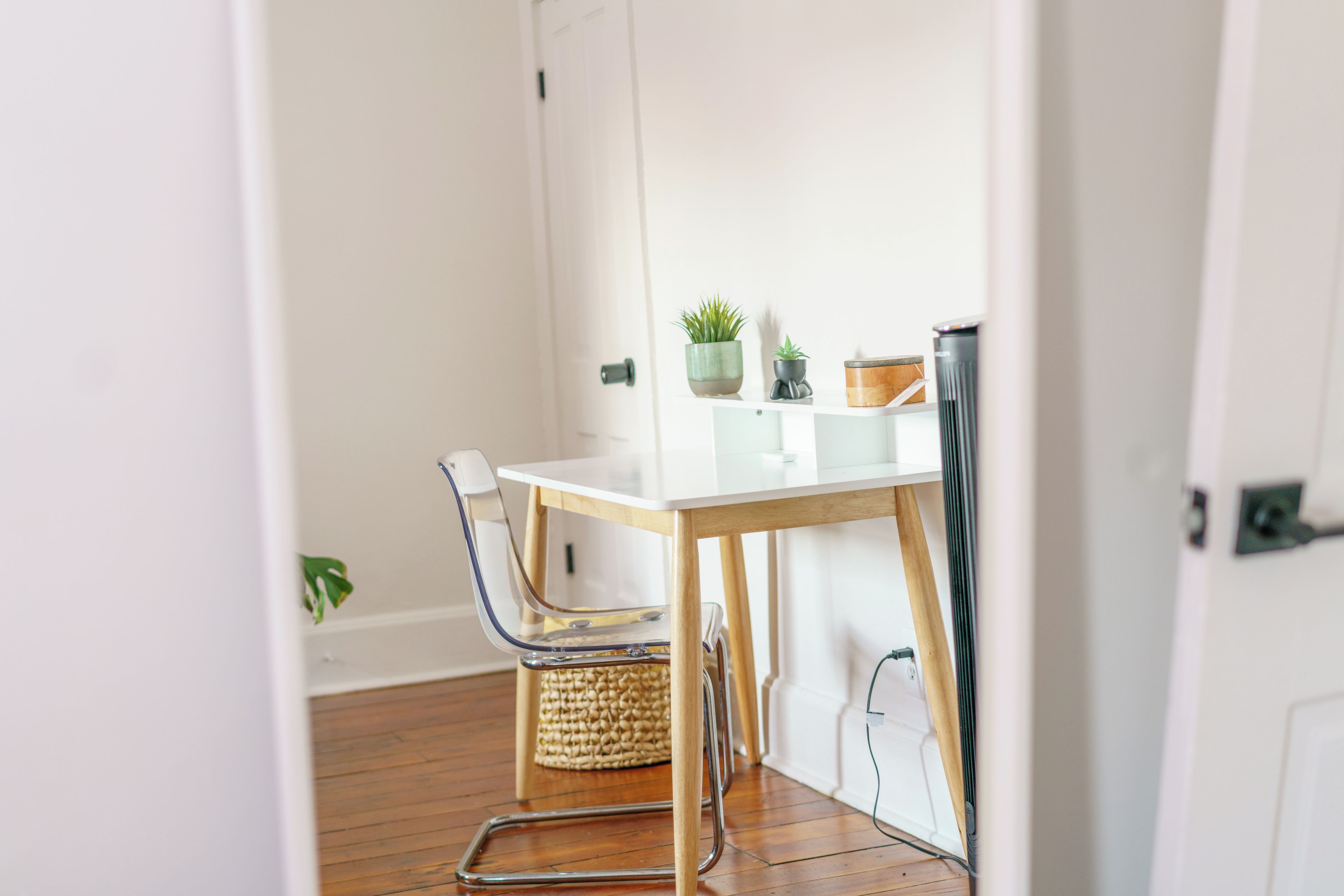 A small, clean room with a white table, a chair, a plant, and a basket.