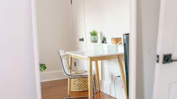 A small, clean room with a white table, a chair, a plant, and a basket.