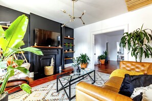 Ein Wohnzimmer mit Kamin, einer Couch, einem Couchtisch und diversen Pflanzen.