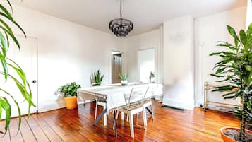 A dining area with a wooden floor, white walls, a chandelier, and potted plants.