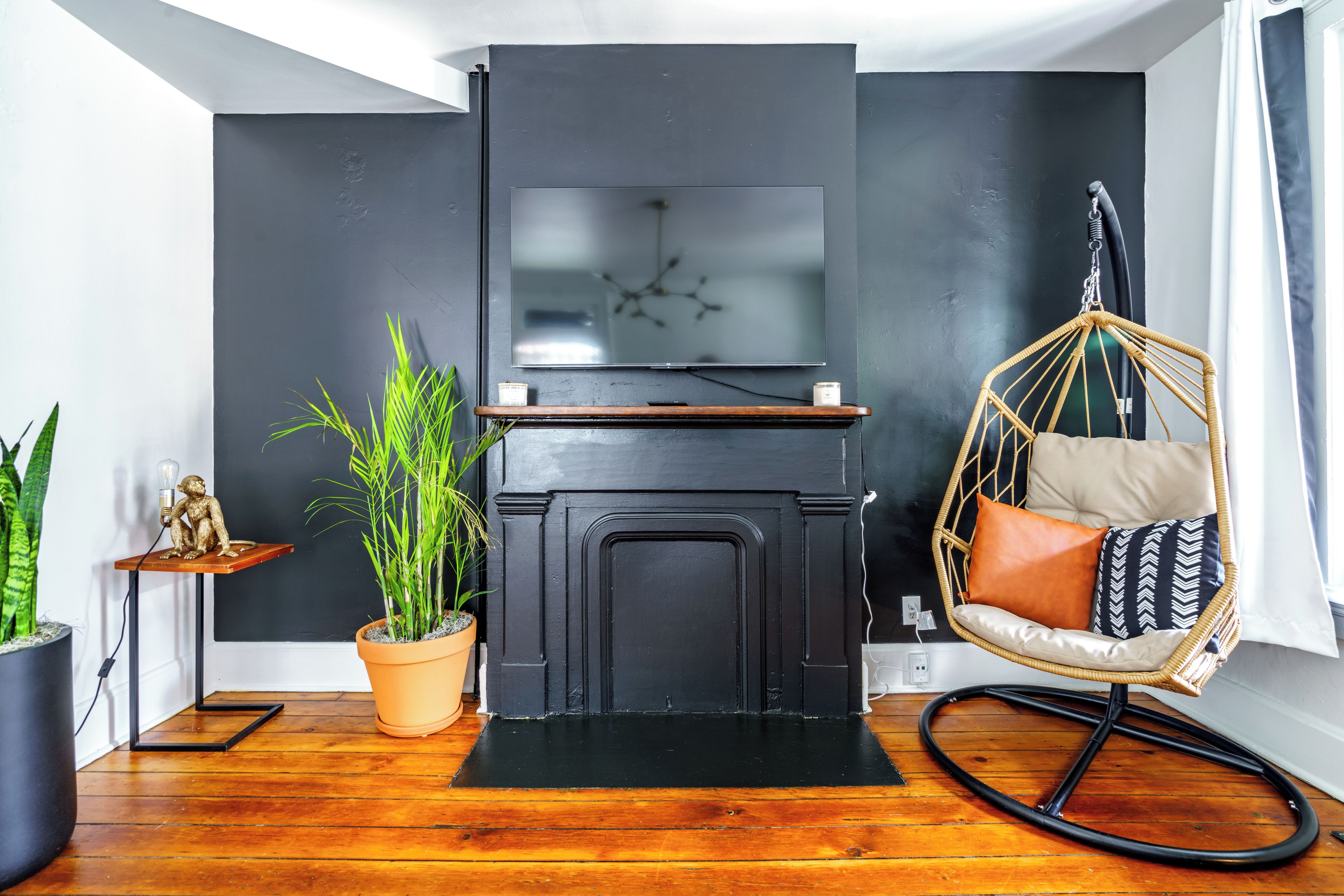 A modern living room with a black fireplace, a hanging chair, and a potted plant.