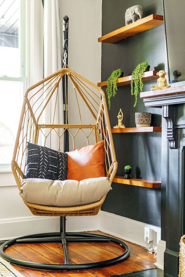 Een kamer met een hangstoel, houten planken en een open haard.