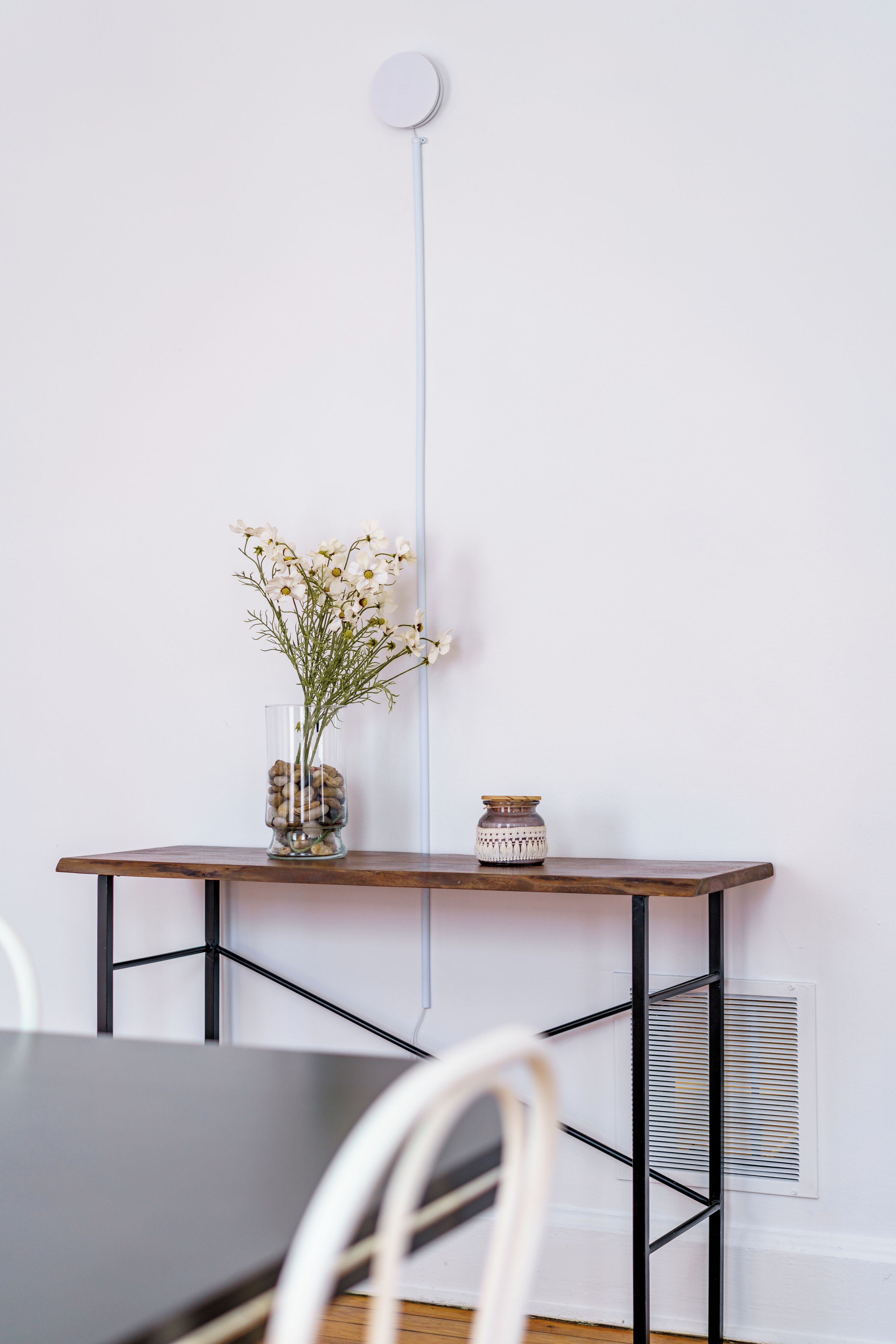 Una habitación minimalista con una mesa de madera, un florero con flores y un pequeño frasco decorativo.