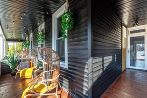 A covered porch with wooden flooring, wicker chairs, and hanging plants. - Jungle House Urban Lofts – Arena District & Short North (Columbus)