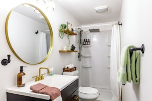 Een badkamer met een witte wastafel, gouden kraanwerk, een grote spiegel, een toilet, een douche en groene handdoeken.