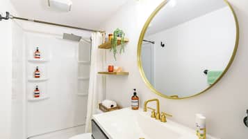 A bathroom with a white sink, gold faucets, a large mirror, and shelves with toiletries.