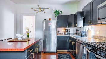 A modern kitchen with a central island, stainless steel appliances, dark cabinetry, and a black and white patterned rug.
