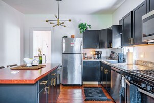 A modern kitchen with a central island, stainless steel appliances, dark cabinetry, and a black and white patterned rug.