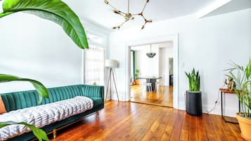 A modern living room with a green sofa, wooden flooring, a unique chandelier, and potted plants.