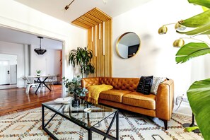 A living room with a brown leather sofa, a glass coffee table, a patterned rug, a wooden accent wall, and a round mirror. - Jungle House Urban Lofts – Arena District & Short North (Columbus)