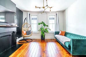 A modern living room with a green sofa, a hanging chair, a potted plant, and a wooden floor. - Jungle House Urban Lofts – Arena District & Short North (Columbus)