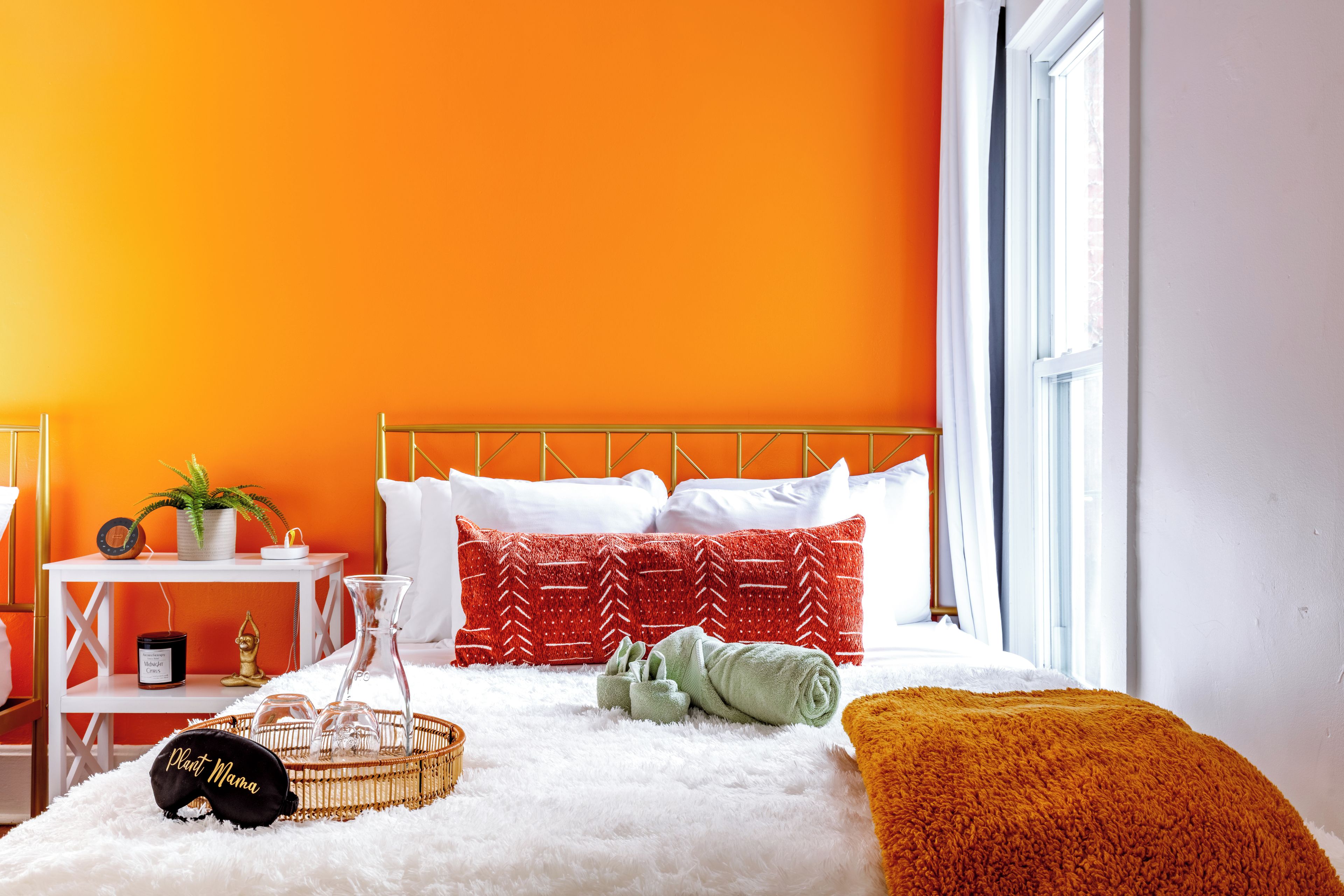 A bedroom with a bed, pillows, a bedside table, a window, and a plant.
