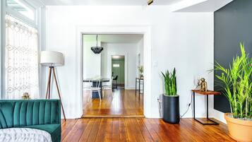 Una sala de estar moderna con un sofá verde, una lámpara de pie, una zona de comedor con mesa y sillas, y un pasillo que conduce a otra habitación.