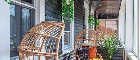 A covered porch with wicker chairs, a small table, and a potted plant.