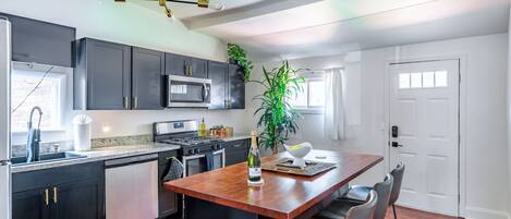 A modern kitchen with dark cabinets, a central island, bar stools, a microwave, and a hanging light fixture.