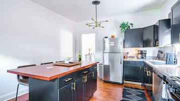 A modern kitchen with a central island, black cabinetry, stainless steel appliances, and a wooden floor.
