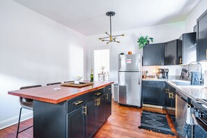 A modern kitchen with a central island, black cabinetry, stainless steel appliances, and a wooden floor. - Jungle House Urban Lofts – Arena District & Short North (Columbus)