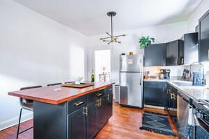 A modern kitchen with a central island, black cabinetry, stainless steel appliances, and a wooden floor.
