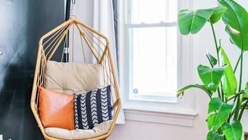 A room with a hanging chair, a potted plant, and a window.