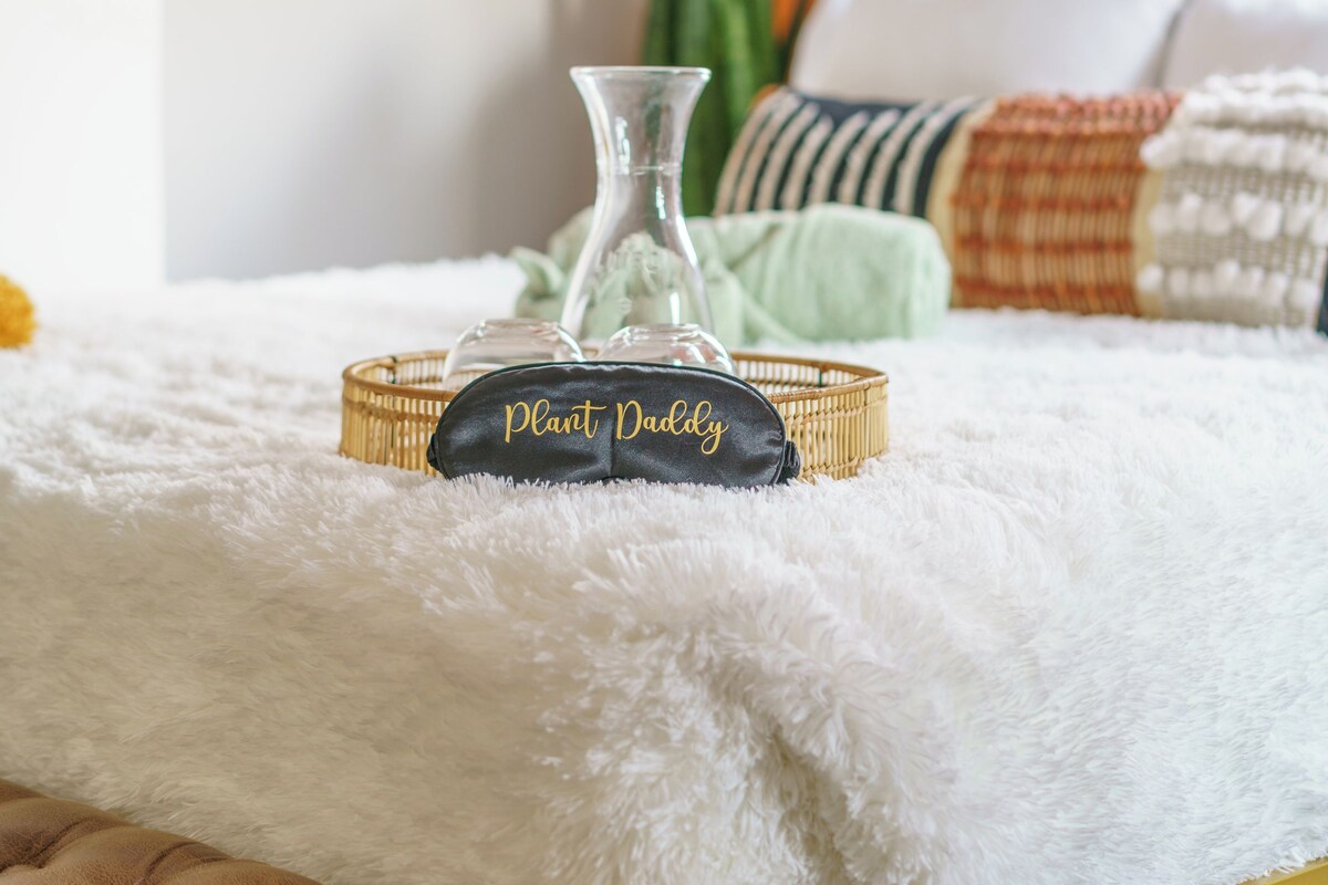 A bed with a white fluffy blanket, a glass vase, and a pillow with 'Peachy Ducky' text.