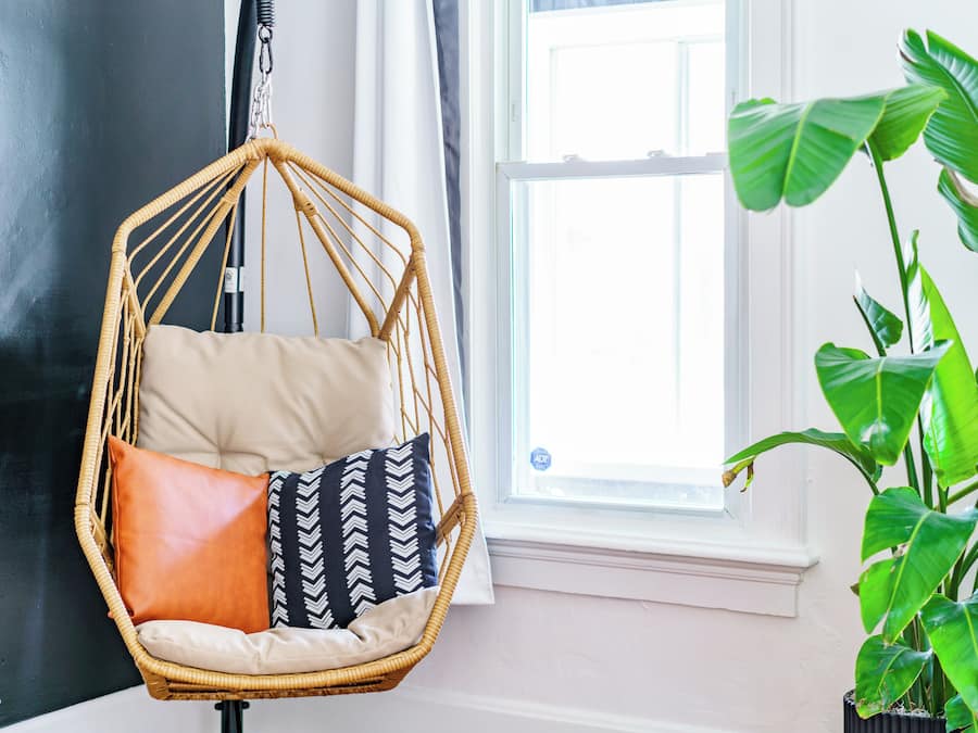 A room with a hanging chair, a potted plant, and a window.