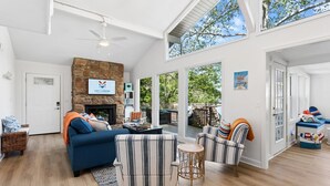 Uma sala de estar ampla com lareira de pedra, um sofá azul, poltronas listradas e um espaço de refeições com vista para o exterior.