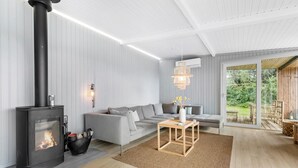 Een moderne woonkamer met een houtkachel, een grijze bank en uitzicht op de omgeving.