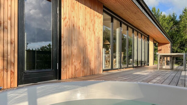 Een modern gebouw met een houten gevel, grote schuifdeuren van glas en een houten terras.