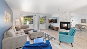 Una sala de estar moderna con un sofá modular, un reposapiés y un sillón azul verdoso. En el centro, una chimenea con revestimiento de piedra.