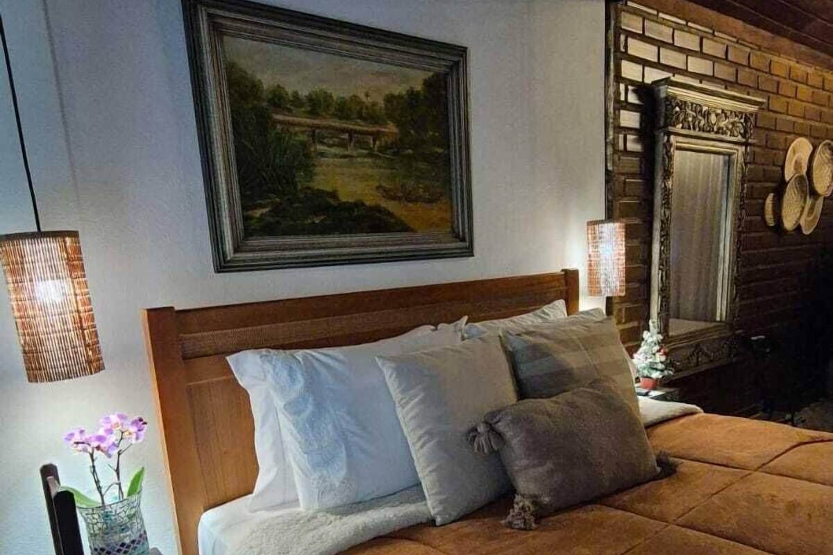 Une chambre avec un grand lit, un tableau au mur, une cheminée en briques et une petite table sur laquelle est posé un vase.