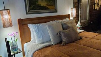 Un dormitorio con una cama grande, un cuadro en la pared, una chimenea de ladrillo y una mesita con un florero.
