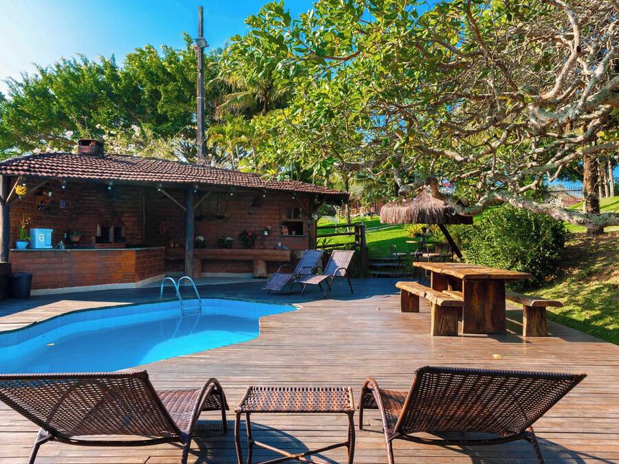 A wooden deck with a swimming pool, lounge chairs, and a thatched-roof structure.