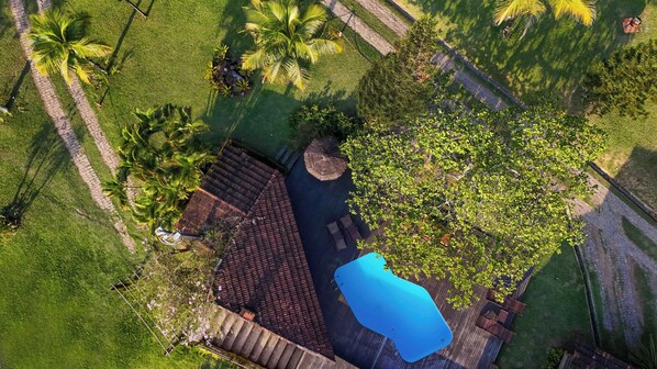 An aerial view of a property with a swimming pool, a wooden deck, and surrounding greenery.