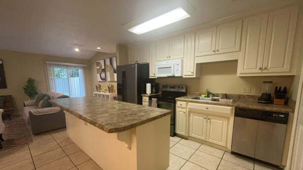 A kitchen with white cabinets, a granite countertop, a refrigerator, an oven, a dishwasher, and a window with blinds. - Stylish 4-bedroom, 3 Bath Townhome in Valdosta (Valdosta)