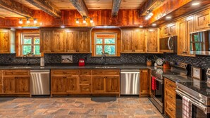 A spacious kitchen with wooden cabinets, a central island, stainless steel appliances, and a black tiled backsplash. - Black Eagle Lodge -  Unique - 8 Bedrooms - 2 Pools (Logan)
